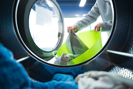 Woman With A Green Basket Taking Clothes Out Of The Washing Machine