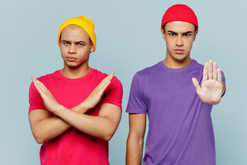 Young strict sad dissatisfied couple two friends men wearing casual clothes looking camera together showing stop gesture with palm isolated on pastel plain light blue cyan background studio portrait.