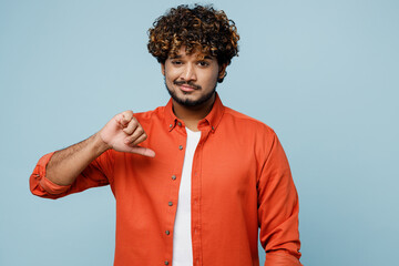 Young sad dissatisfied displeased Indian man wear orange red shirt white t-shirt show thumb down...