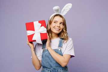Young fun woman wearing casual clothes bunny rabbit ears hold in hand present box with gift ribbon bow isolated on plain pastel light purple background studio portrait. Lifestyle Happy Easter concept.