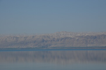 Panoramic view of the beautiful, clear blue Dead Sea shimmering and shining on a bright sunny day in Jordan and the dry land around it.