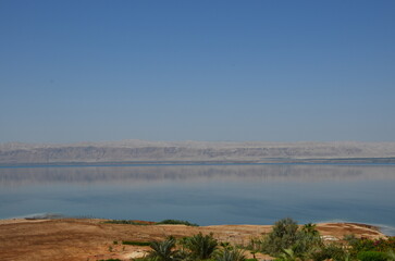 Fototapeta na wymiar Panoramic view of the beautiful, clear blue Dead Sea shimmering and shining on a bright sunny day in Jordan and the dry land around it.