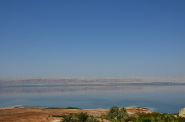 Panoramic view of the beautiful, clear blue Dead Sea shimmering and shining on a bright sunny day in Jordan and the dry land around it.