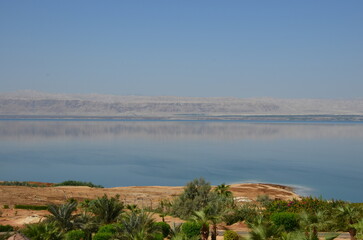 Panoramic view of the beautiful, clear blue Dead Sea shimmering and shining on a bright sunny day in Jordan and the dry land around it.