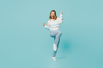 Full body overjoyed excited young woman wear striped hoody doing winner gesture celebrate clenching fists say yes isolated on plain pastel light blue cyan background studio portrait Lifestyle concept