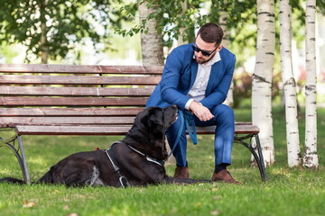 Young man in business suit wearing sunglasses speaking with his dog at walk