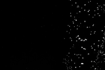 Shiny air bubbles in the right side of the frame on a black isolated background. Background with oxygen bubbles and workspace, mockup. Close up of a bubbling liquid. Fizzy flow of air bubbles.