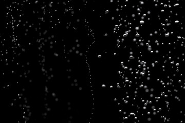 Naklejka na ściany i meble Shiny air bubbles underwater rising from bottom and illuminated by rays of light. Stream of oxygen bubbles on a black isolated background. Close up of a bubbling liquid during aeration of water.