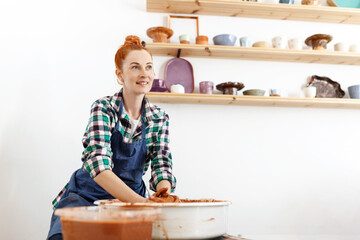 Happy female sculptor making clay pot on pottery wheel