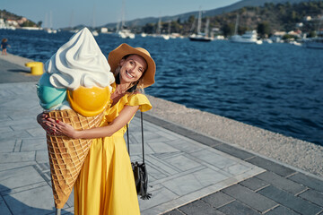 Summer desert. Outdoor portrait of happy pretty young woman holding giant icecream cone on the sea...
