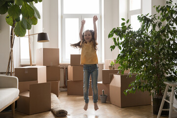 Fototapeta na wymiar Happy excited kid girl playing among cardboard boxes, dancing, jumping, celebrating relocation, moving into new apartment, home, flat, having fun, enjoying activity
