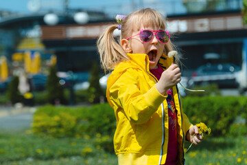 Cute little girl in pink sunglasses blowing a dandelion outdoors.