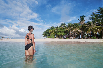Vacation on the seashore. Back view of young woman swimming on the beautiful white sand beach tropical island.