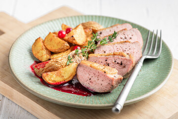 Roast duck breast with potatoes and berry sauce on a serving board, selective focus