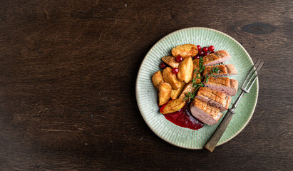 Roasted duck breast with potatoes, berry sauce and thyme on a wooden background, top view, copy...