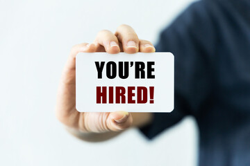 You're hired text on blank business card being held by a woman's hand with blurred background....