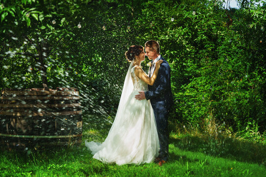 a bride and groom is dancing happily in garden under water drops