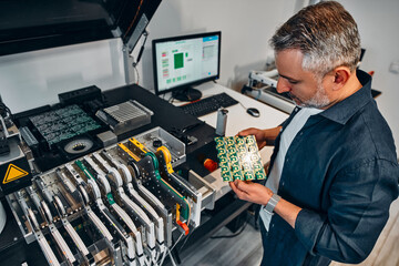 A man holds a microcircuit near a machine that develops chips for electronics maintenance.