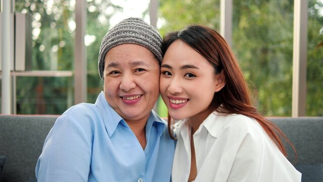 Close Up Smiling Face Of Asian Granddaughter And Grandmother Patient Looking At Camera On Sofa At Home