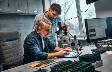 Two men work in a modern office on the development of microchips for the maintenance of electronic...