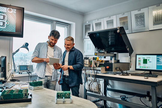 Two men are standing in an office and looking at a tablet, many chips in the background.Concept of engineering, chip development and service.