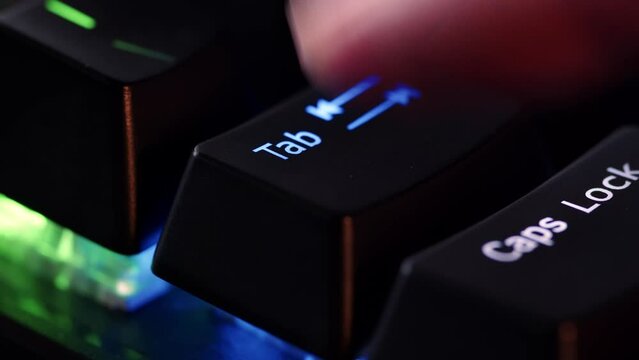 Human finger is clicking on the Tab button on the computer keyboard, close up view. The finger presses Tab on the keyboard key, macro shot. Loop footage.