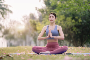 Fototapeta premium Asian young women practicing yoga In the prayer position and raised hands while sitting on mat at park, Concept of relaxation and meditation.