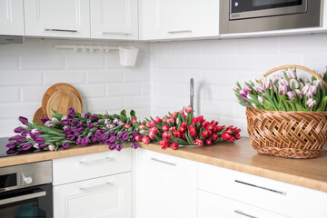 A large number of tulips of different colors lies on the table in the kitchen. Flowers in the sink