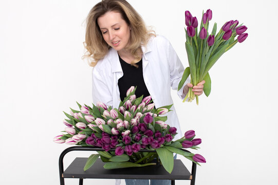 Cute florist girl in a shirt collects a bouquet of purple and white tulips for a birthday present