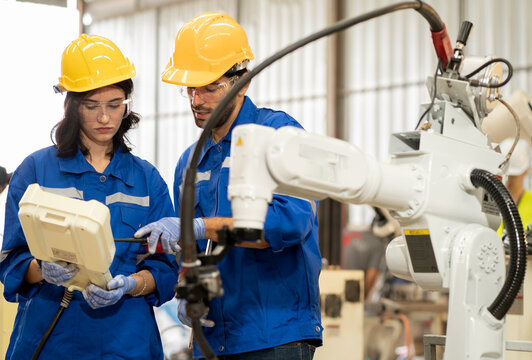 Female industrial engineer using remote control board to control robotic welder operation in modern automation factory. Technician worker monitoring robot controller system for automated steel welding