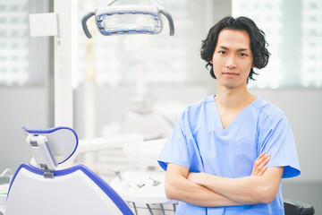 歯科治療ユニットの前で腕組みをする若い男性歯科医師