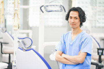 歯科治療ユニットの前で腕組みをする若い男性歯科医師