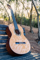 Beautiful classical guitar on a bench in the park with lens flare. Photo of a new wooden guitar with nylon strings outdoors in the summer during sunset. No people. Beautiful string instrument.