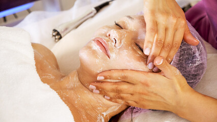 Cosmetologist applies  a moisturizing mask on female face. Woman in a spa salon on cosmetic...