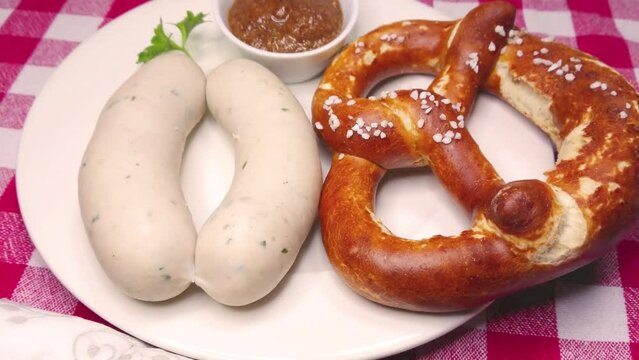 Two munich white sausages, pretzel and sweet bavarian mustard, rotating on plate