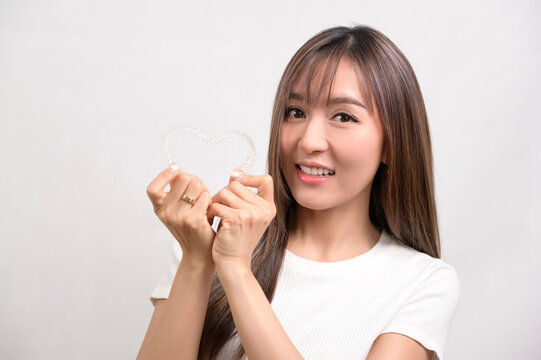 Young smiling woman holding invisalign braces over white background studio, dental healthcare and Orthodontic concept..
