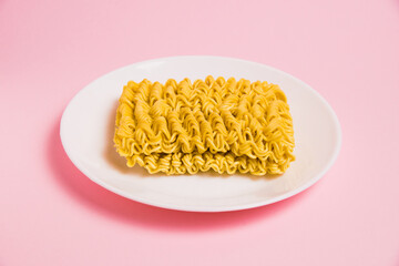 Instant noodles in a white plate on a pink background. Fast food in the modern world.