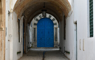 Fototapeta na wymiar Alley in Tunis Medina with Traditional Blue Door with Black and White Arch at the End
