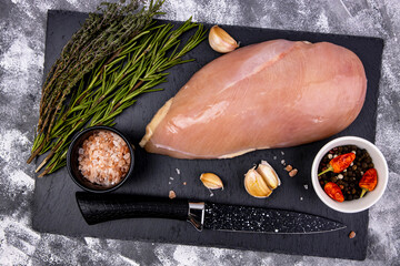 Seasoned chicken breast on cutting stone board with spices, top view, raw diet chicken breast