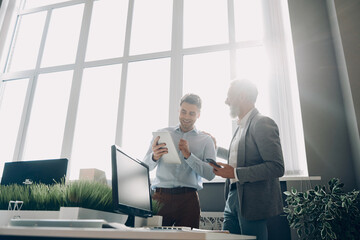 Two happy men discussing business while working in the office together