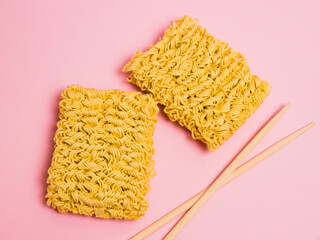 Large serving of raw instant noodles and chopsticks on pink paper background with copy space