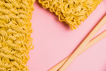 Large serving of raw instant noodles and chopsticks on pink paper background with copy space