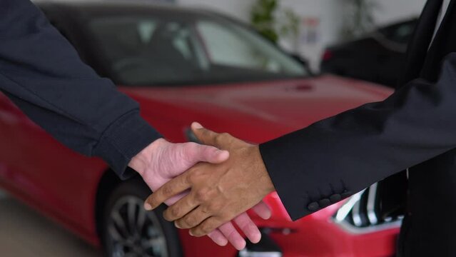 Indian car manager giving keys to customer at salon. Two men shaking hands for making deal. Close up of hands, blur background. Concept of car selling. Right hand drive car