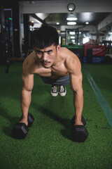 A determined guy does a set of dumbbell push-ups at the gym. Upper body and chest workout. Shirtless revealing a defined and muscular physique.