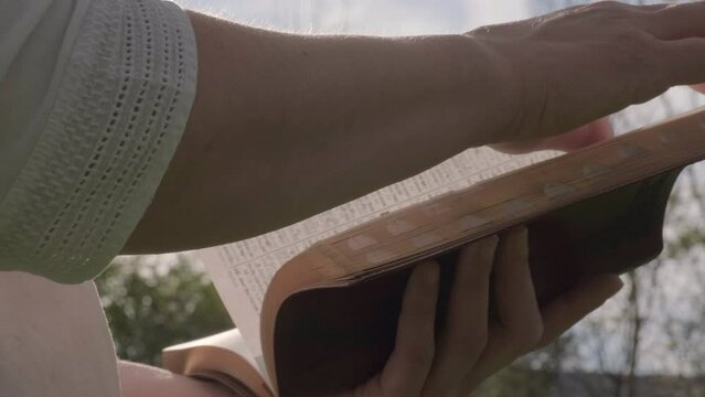 Woman's Hand Turning Bible Page Close Up Slow Motion Outside Sunny Day