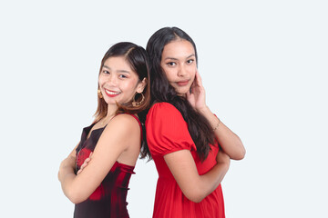 Two attractive Gen Z Filipina women posing back to back with arms crossed. Late teens to early 20s and wearing red casual outfits. Teamwork concept. Isolated on a white background.