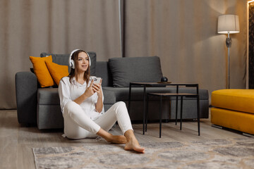 Obraz premium Teen student girl wear headphones using smartphone and watching online video course at home