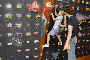 Fototapeta Kid girl at climbing wall with male instructor in climbing center obraz