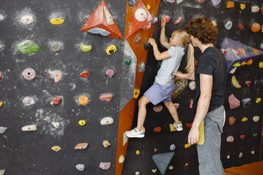 Kid girl at climbing wall with male instructor in climbing center