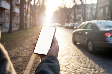 Smartphone blank screen in hand of man on sunset in town background.